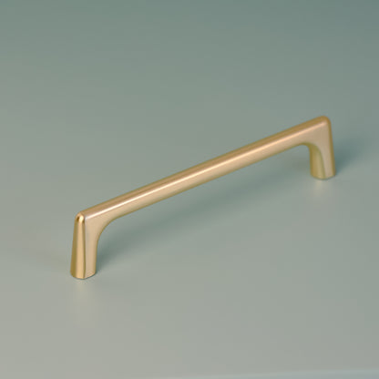 Darwin 128mm cabinet handle in brushed brass finish, displayed on a soft green background, showcasing its sleek, minimalist design and gently curved edges.